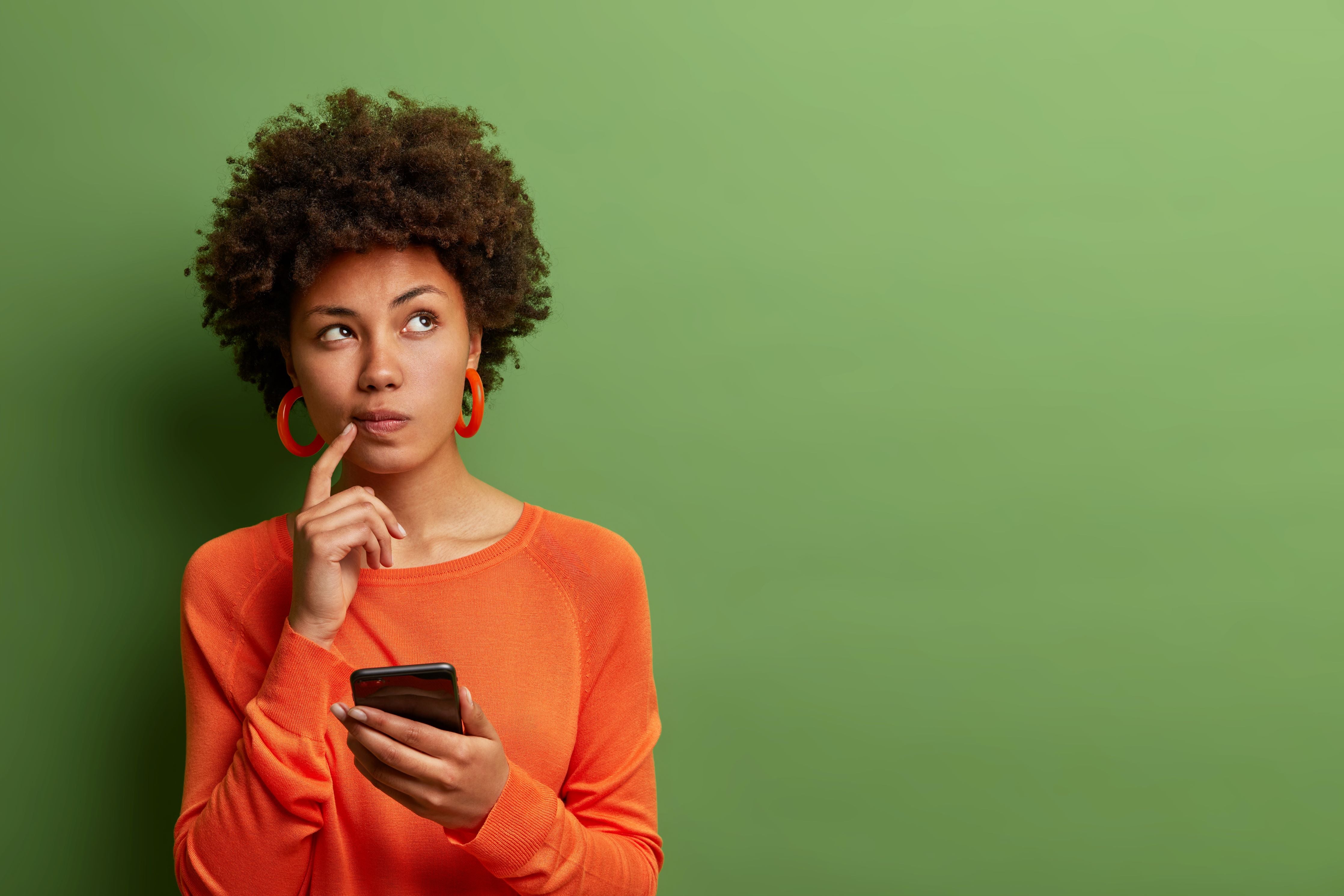 Woman with a cellphone thinking deeply with her finger on the chin and a green background 