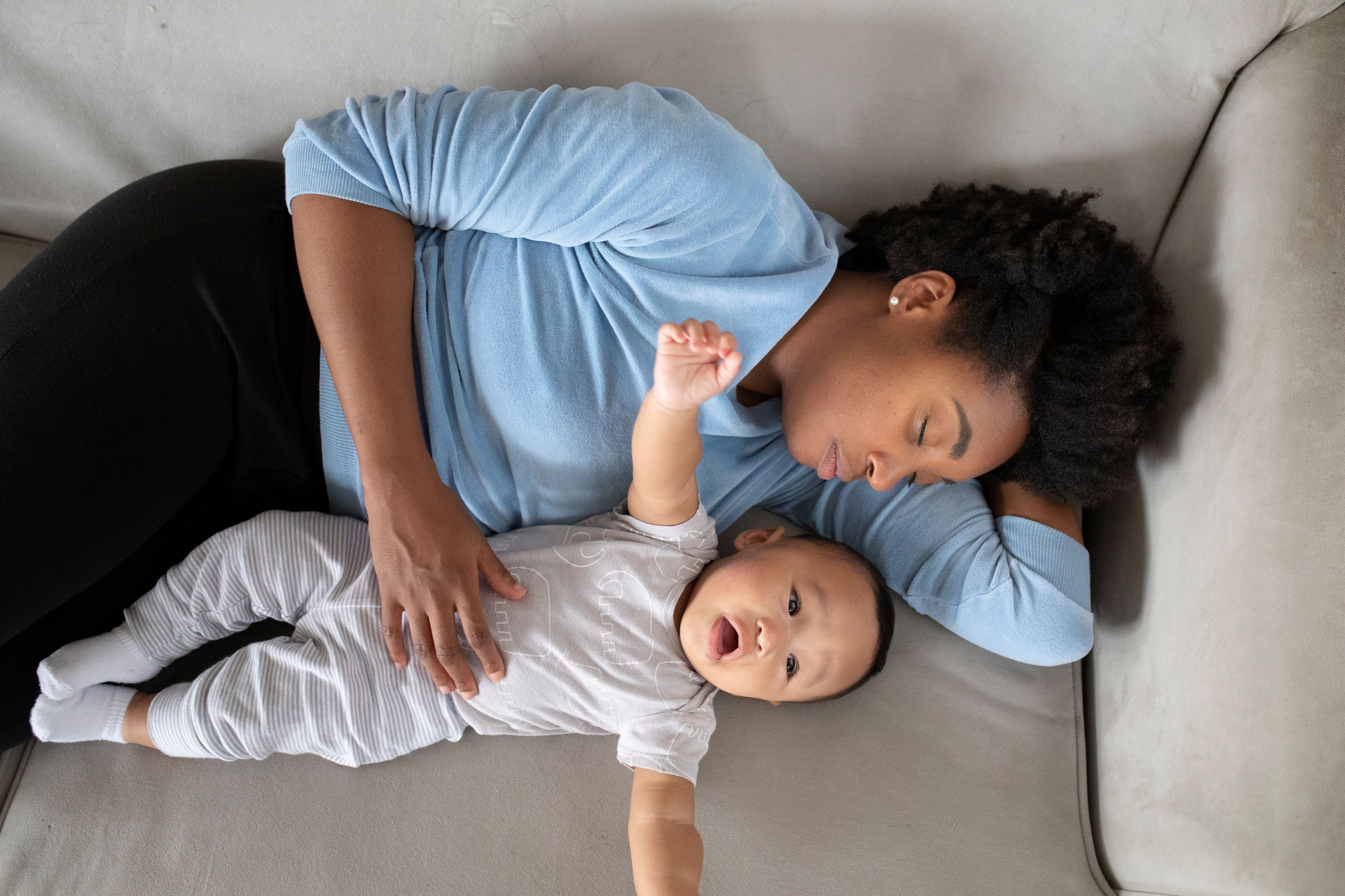 Tired woman sleeping on a couch while holding her baby