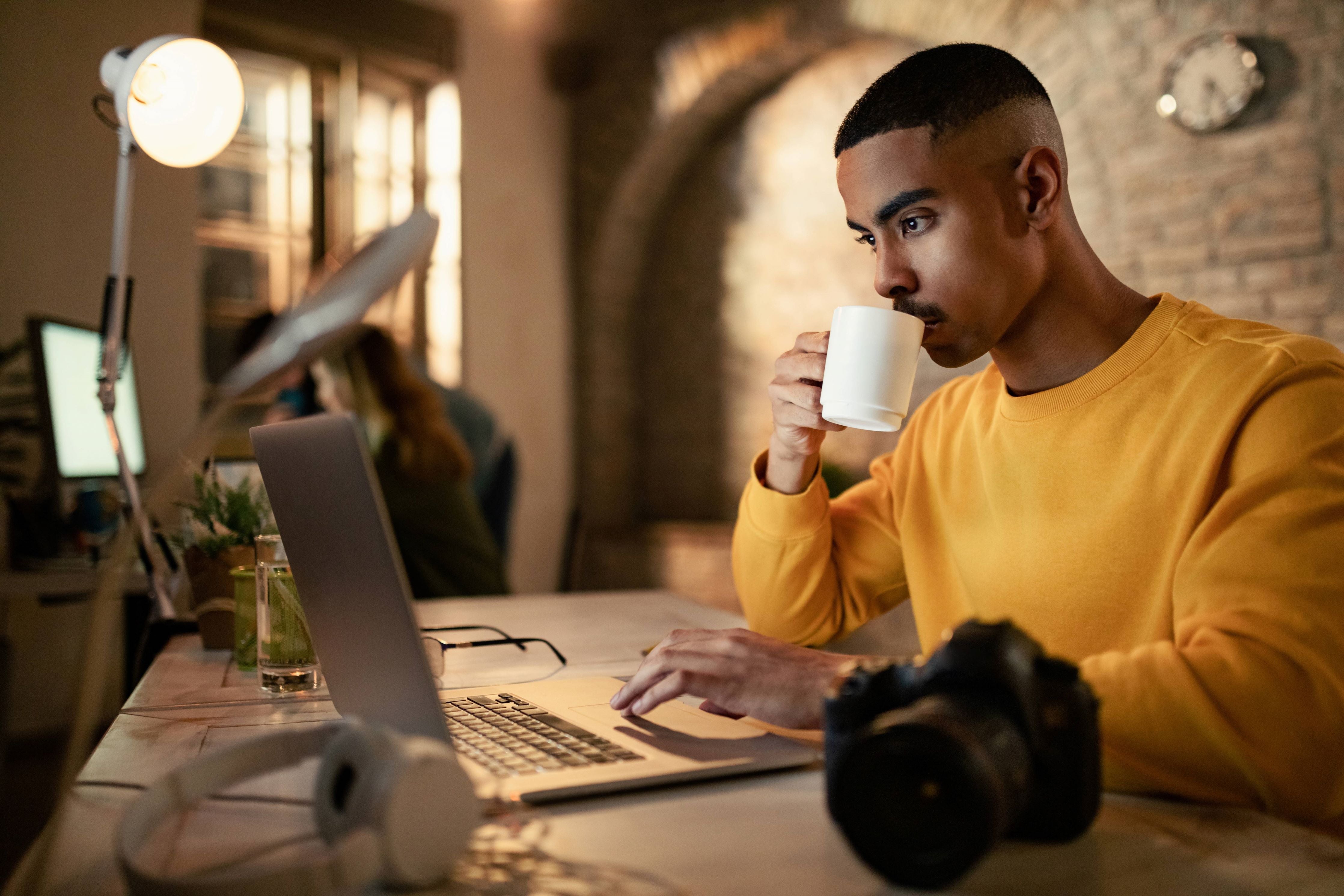 Young Professional man drinking tea on a white cup while working on his computer in a cafe